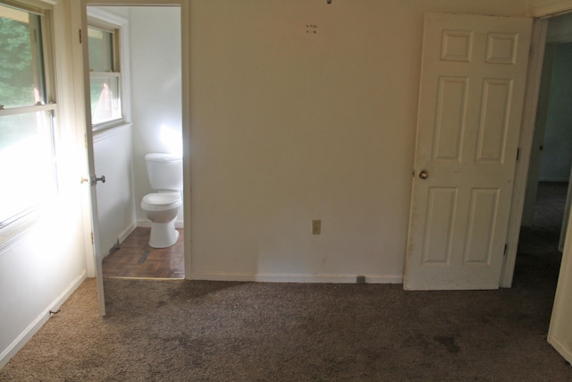 unfurnished bedroom featuring dark carpet and ensuite bathroom