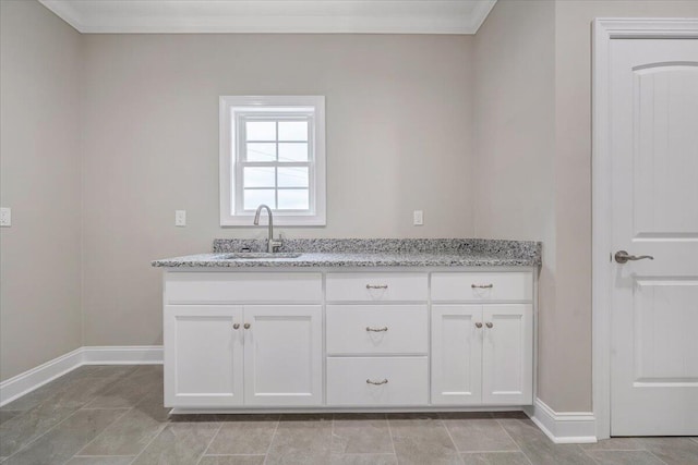 kitchen with light stone counters, white cabinetry, sink, and ornamental molding