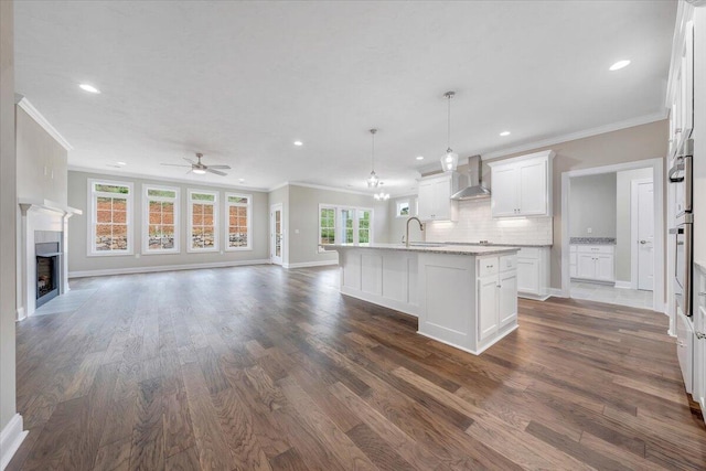 kitchen featuring plenty of natural light, an island with sink, dark hardwood / wood-style floors, and wall chimney range hood