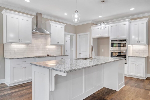 kitchen with white cabinets, an island with sink, dark hardwood / wood-style floors, and wall chimney range hood