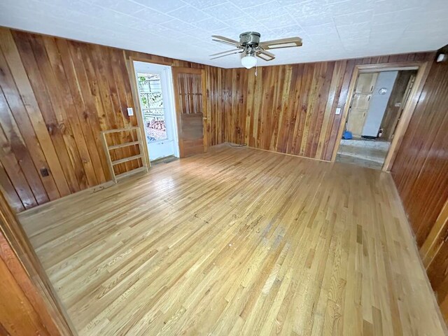 unfurnished room featuring ceiling fan, wooden walls, and light hardwood / wood-style floors