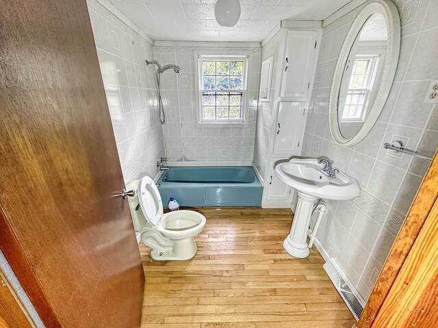 bathroom with wood-type flooring, tiled shower / bath, tile walls, and toilet