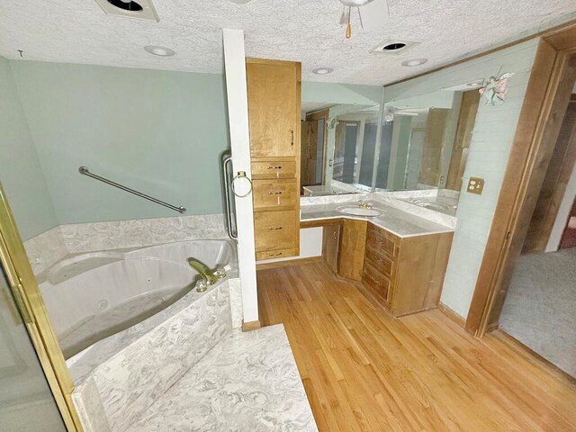 bathroom with a textured ceiling, hardwood / wood-style floors, ceiling fan, vanity, and a bathing tub