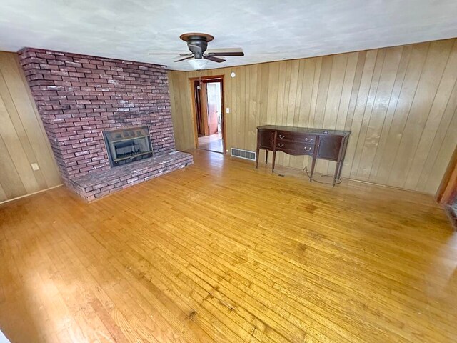 unfurnished living room with light wood-type flooring, wood walls, ceiling fan, and a fireplace