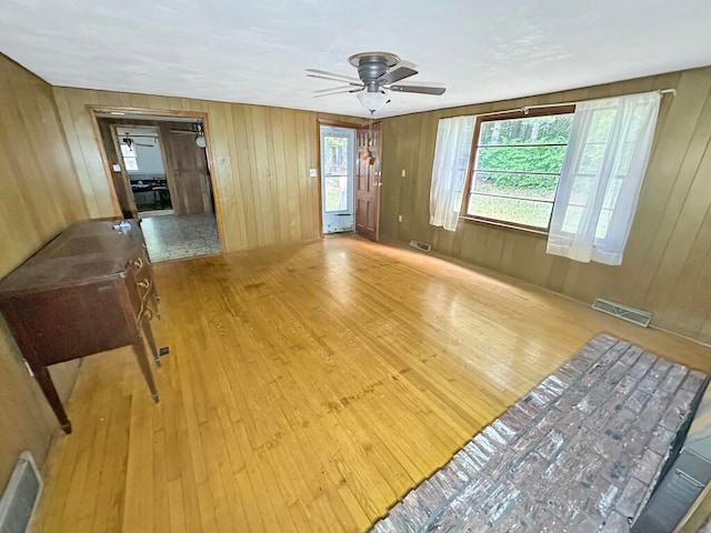 unfurnished room with ceiling fan, light wood-type flooring, and wood walls