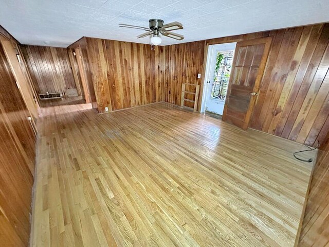 unfurnished room featuring light wood-type flooring, wood walls, and ceiling fan