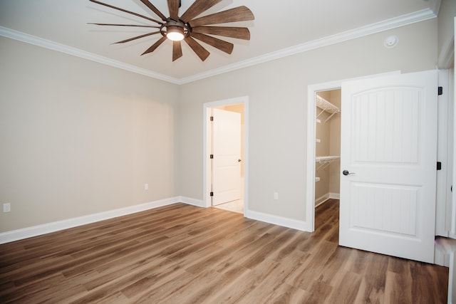 unfurnished bedroom featuring a closet, wood-type flooring, crown molding, ceiling fan, and a walk in closet