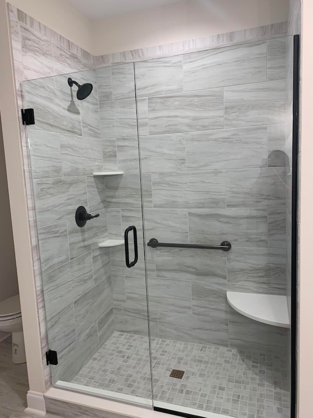 bathroom featuring a shower with door and toilet