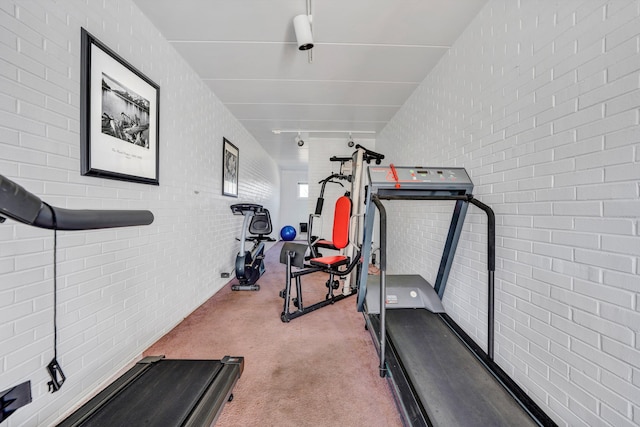 workout area featuring light carpet and brick wall