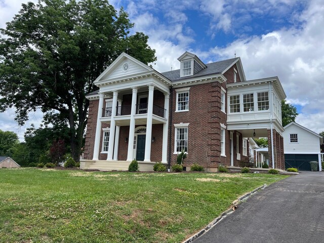 neoclassical / greek revival house featuring a balcony, a garage, an outdoor structure, and a front lawn