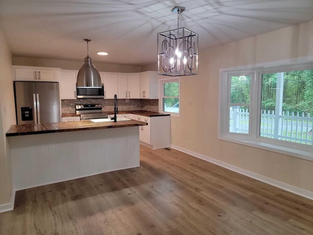 kitchen featuring appliances with stainless steel finishes, a healthy amount of sunlight, white cabinetry, and a notable chandelier