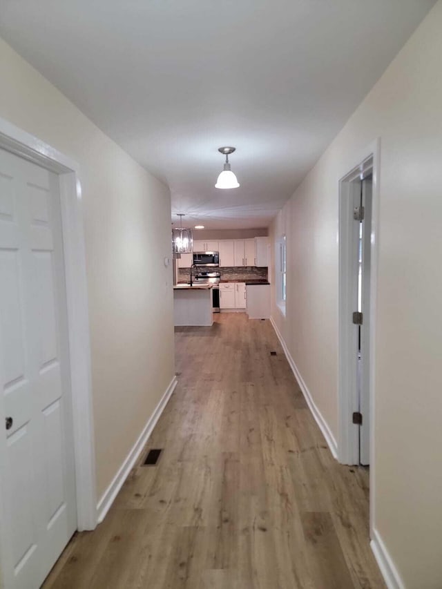 hall with light wood-type flooring and an inviting chandelier