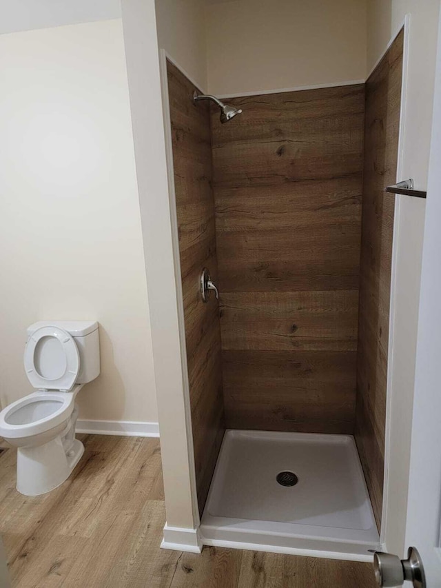 bathroom with hardwood / wood-style flooring, toilet, and tiled shower