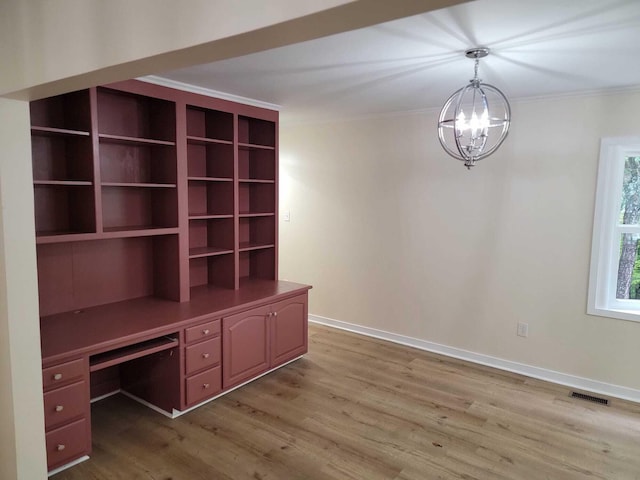 unfurnished office featuring hardwood / wood-style flooring, built in desk, crown molding, and a notable chandelier