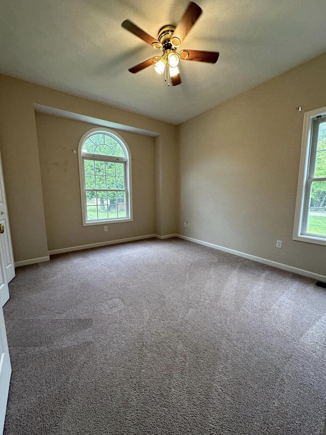 empty room featuring a wealth of natural light, ceiling fan, and carpet flooring