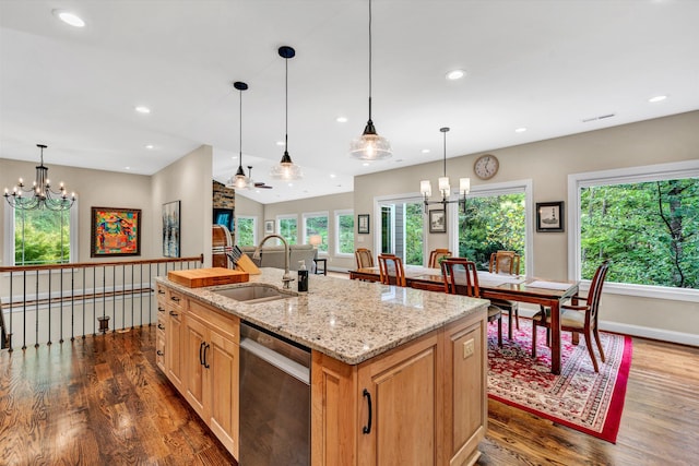 kitchen featuring dark wood-type flooring, an island with sink, an inviting chandelier, stainless steel dishwasher, and light stone counters