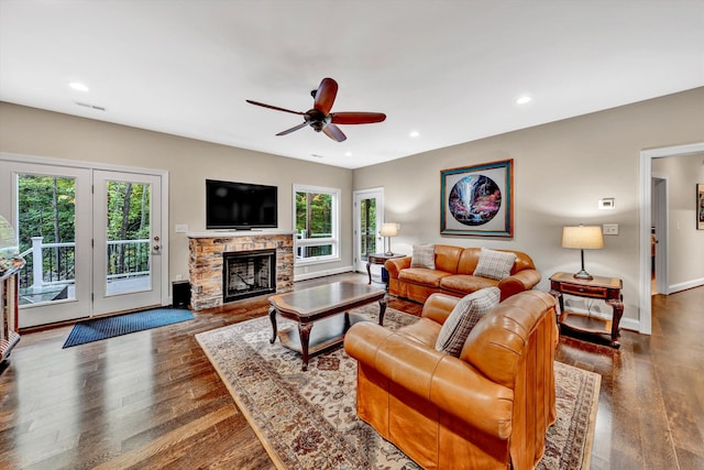 living room featuring ceiling fan, a stone fireplace, and dark hardwood / wood-style flooring