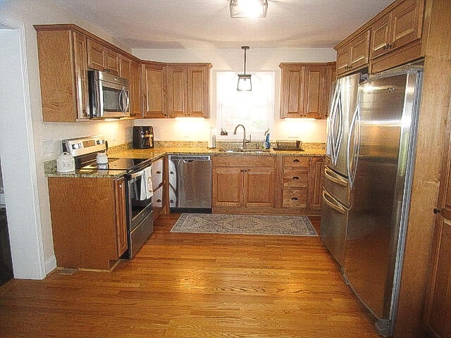 kitchen featuring dark hardwood / wood-style flooring, light stone countertops, sink, and appliances with stainless steel finishes