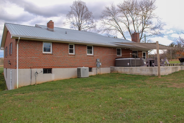 back of property with a yard, a hot tub, and central air condition unit