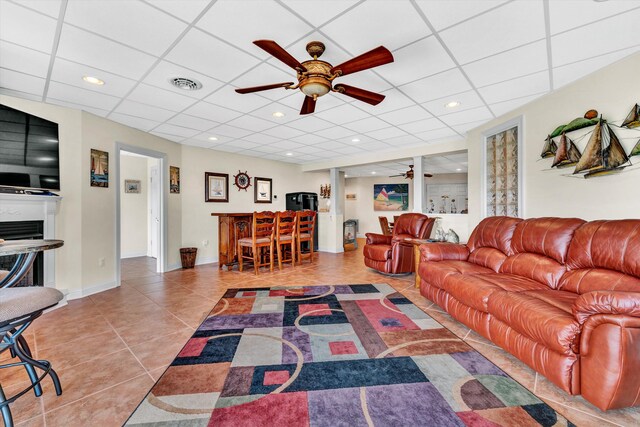 tiled living room featuring ceiling fan, a fireplace, and a paneled ceiling