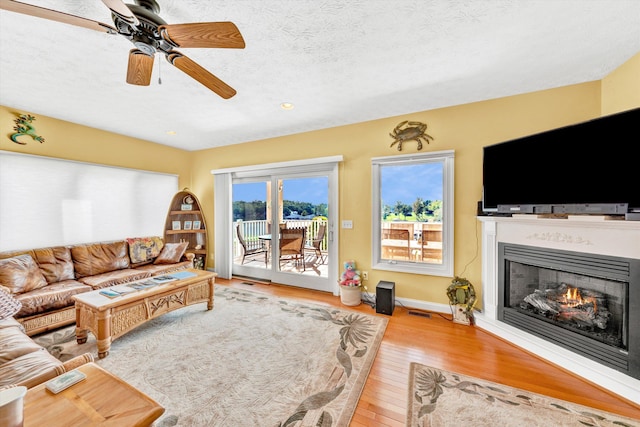 living room featuring light hardwood / wood-style floors, ceiling fan, and a textured ceiling