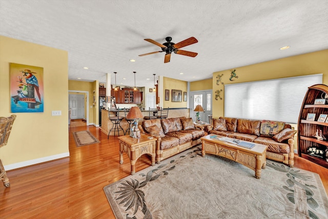 living room featuring light wood-type flooring, a textured ceiling, and ceiling fan