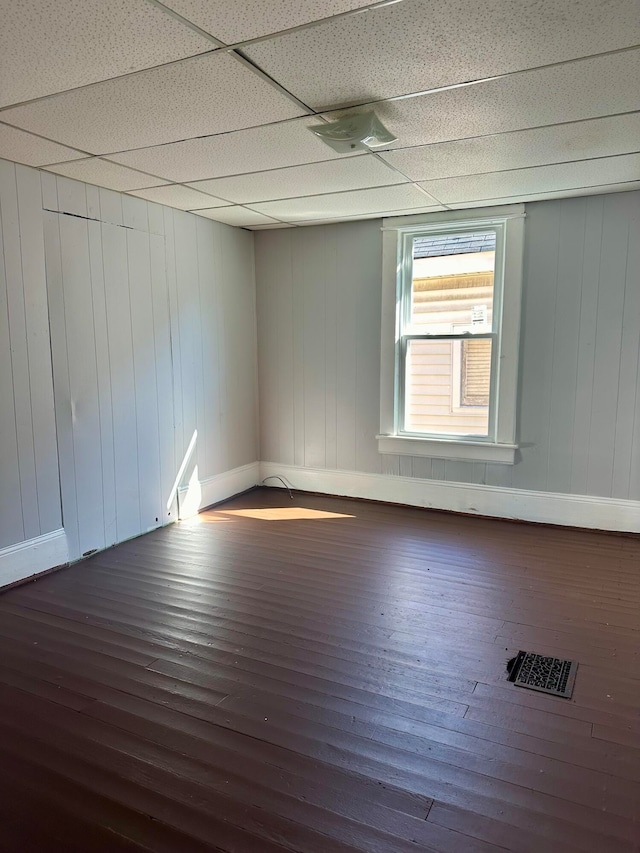 unfurnished room featuring wooden walls, a drop ceiling, and dark hardwood / wood-style floors