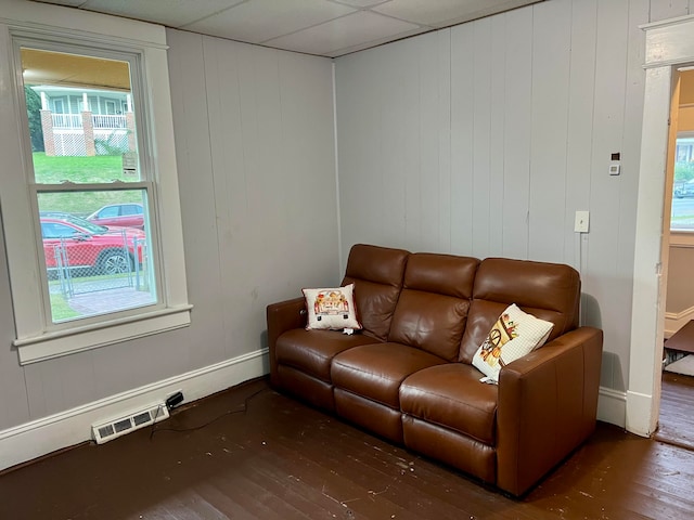 living room featuring a drop ceiling, wood walls, and dark hardwood / wood-style flooring