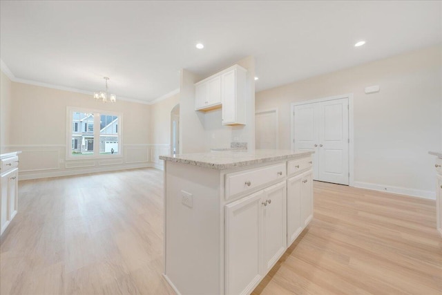 kitchen featuring a kitchen island, light stone countertops, light wood-type flooring, white cabinetry, and pendant lighting