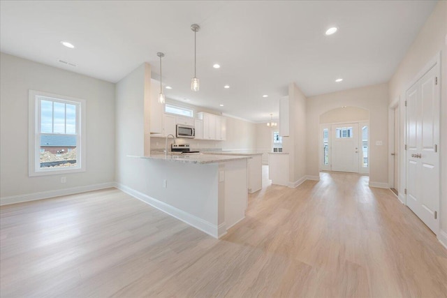 kitchen with a peninsula, light stone countertops, stainless steel appliances, white cabinetry, and pendant lighting