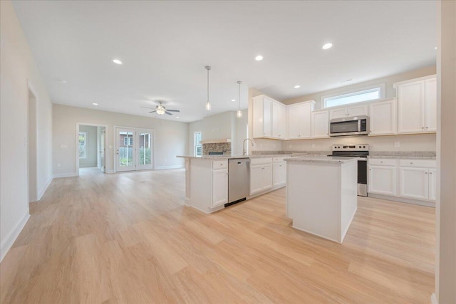 kitchen featuring stainless steel appliances, hanging light fixtures, open floor plan, white cabinets, and a peninsula