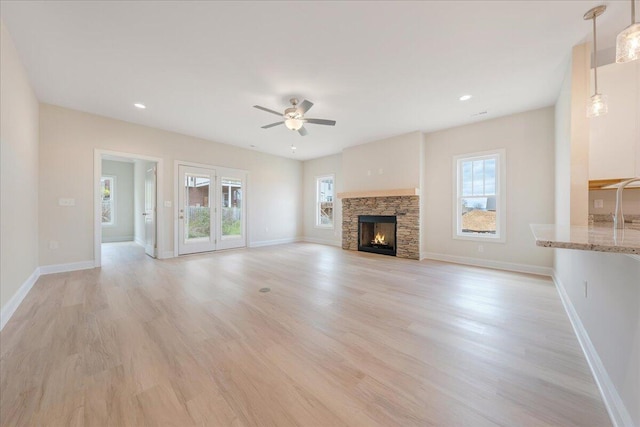 unfurnished living room with light wood-style floors, a stone fireplace, baseboards, and a ceiling fan