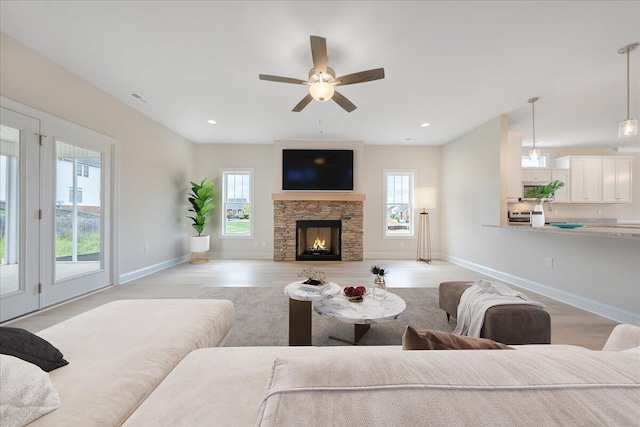 living area with a stone fireplace, recessed lighting, a wealth of natural light, and baseboards