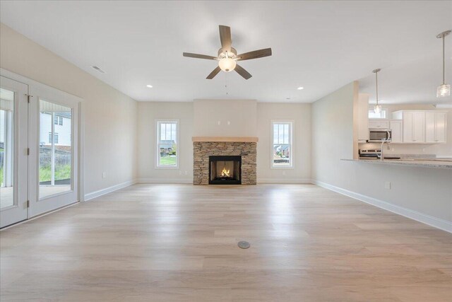 living room featuring ceiling fan, a stone fireplace, plenty of natural light, and light hardwood / wood-style floors