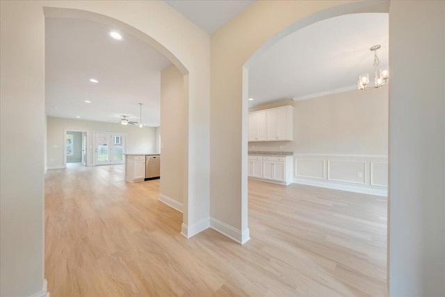 corridor with light wood-style floors, baseboards, a chandelier, and arched walkways