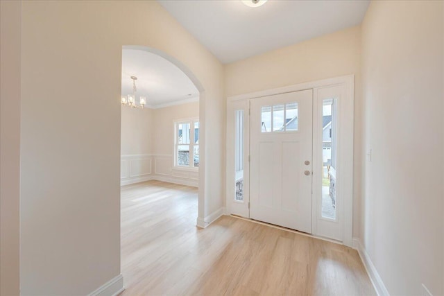 entrance foyer with arched walkways, a decorative wall, a wainscoted wall, light wood-style floors, and an inviting chandelier