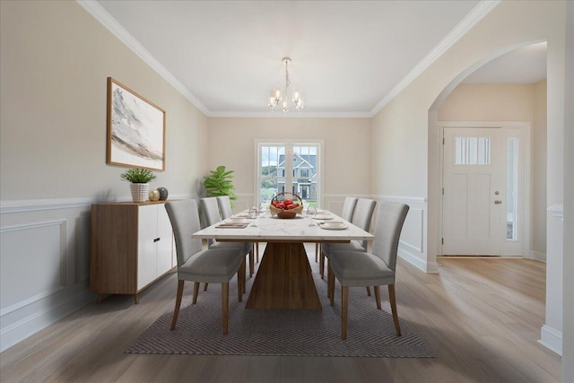 dining area featuring a wainscoted wall, ornamental molding, arched walkways, and wood finished floors