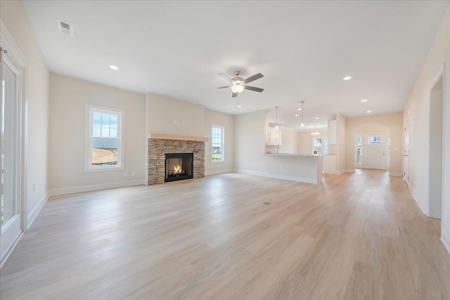 unfurnished living room featuring light wood-type flooring, a stone fireplace, and ceiling fan