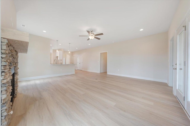 unfurnished living room featuring light hardwood / wood-style flooring, ceiling fan, sink, and a stone fireplace