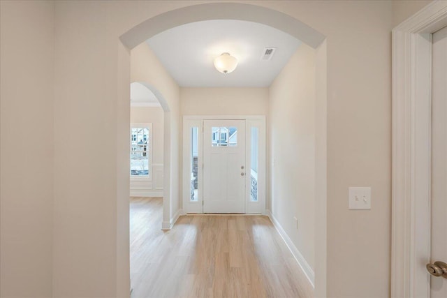entrance foyer with baseboards, arched walkways, light wood-type flooring, and visible vents