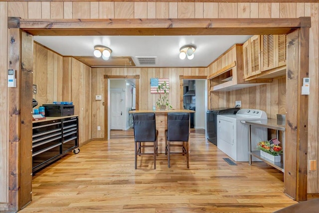 kitchen with a kitchen breakfast bar, wood walls, light hardwood / wood-style flooring, and washer and clothes dryer