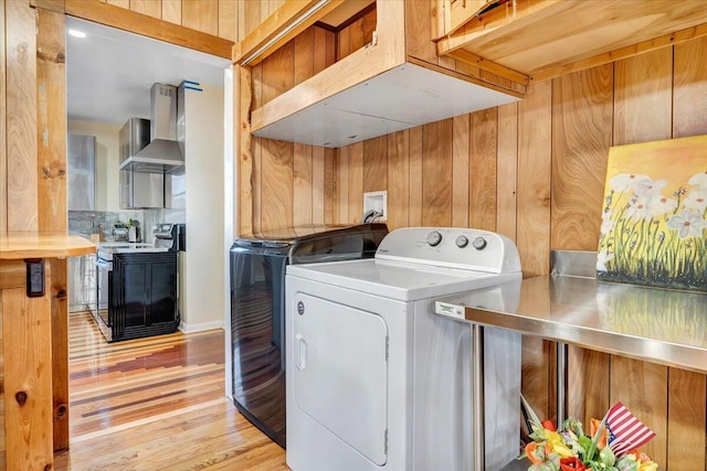 clothes washing area with light hardwood / wood-style flooring, wood walls, and washing machine and dryer