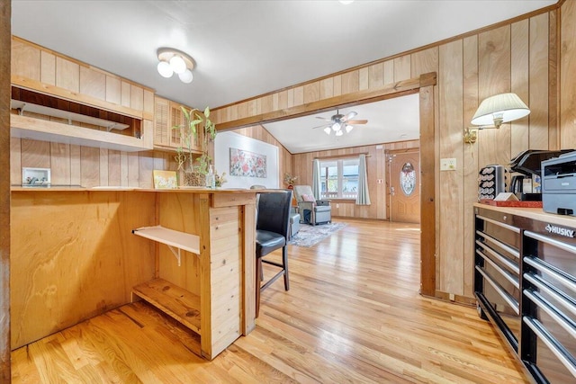 kitchen featuring a breakfast bar, kitchen peninsula, wood walls, light wood-type flooring, and ceiling fan