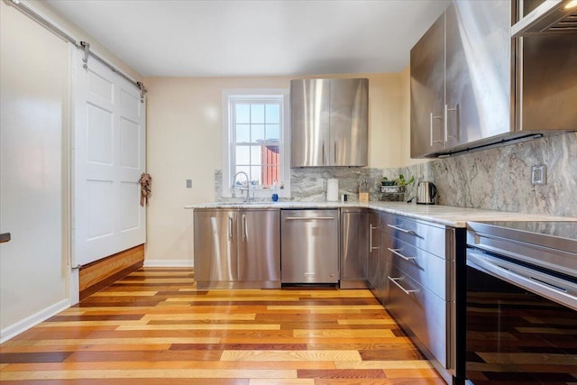 kitchen with light stone countertops, stainless steel appliances, light hardwood / wood-style floors, and tasteful backsplash