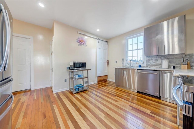 kitchen with light wood-type flooring, light stone counters, tasteful backsplash, sink, and appliances with stainless steel finishes