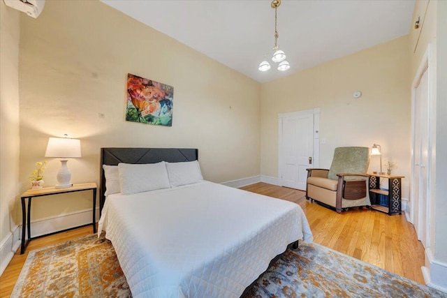 bedroom featuring light hardwood / wood-style flooring, a wall mounted air conditioner, and a notable chandelier