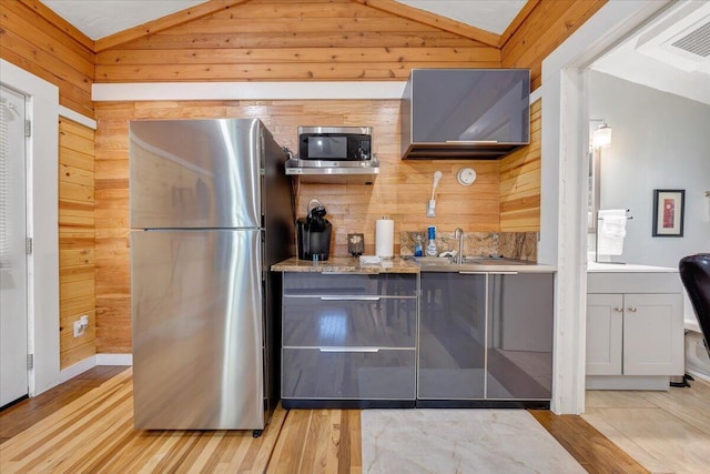 kitchen with light stone counters, lofted ceiling, wooden walls, appliances with stainless steel finishes, and light wood-type flooring