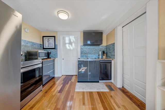 kitchen featuring gray cabinets, light wood-type flooring, sink, backsplash, and appliances with stainless steel finishes