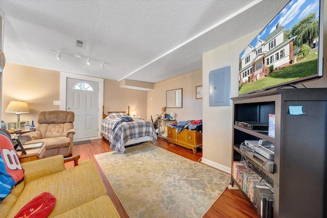 bedroom with wood-type flooring, a textured ceiling, and electric panel