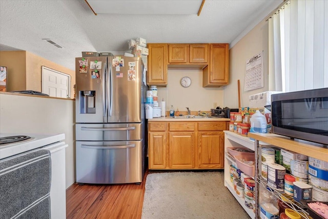 kitchen featuring appliances with stainless steel finishes, a textured ceiling, light hardwood / wood-style floors, and sink